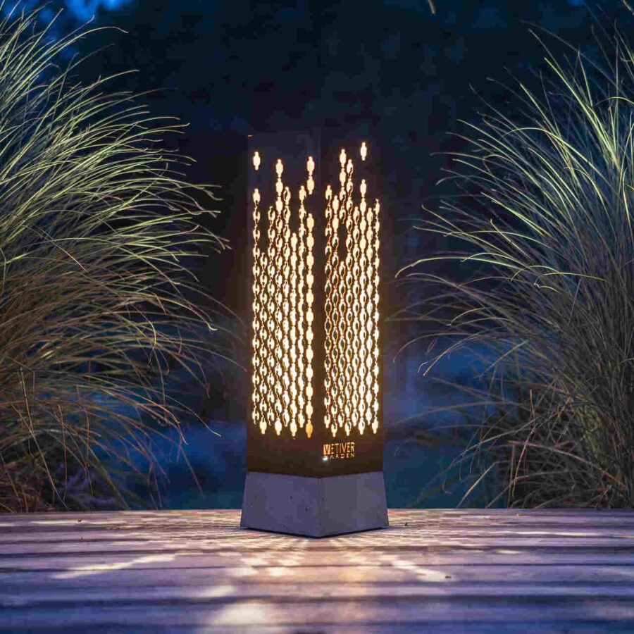 Lampa zewnętrzna, stojąca na drewnianym tarasie wśród rozświetlonych traw.