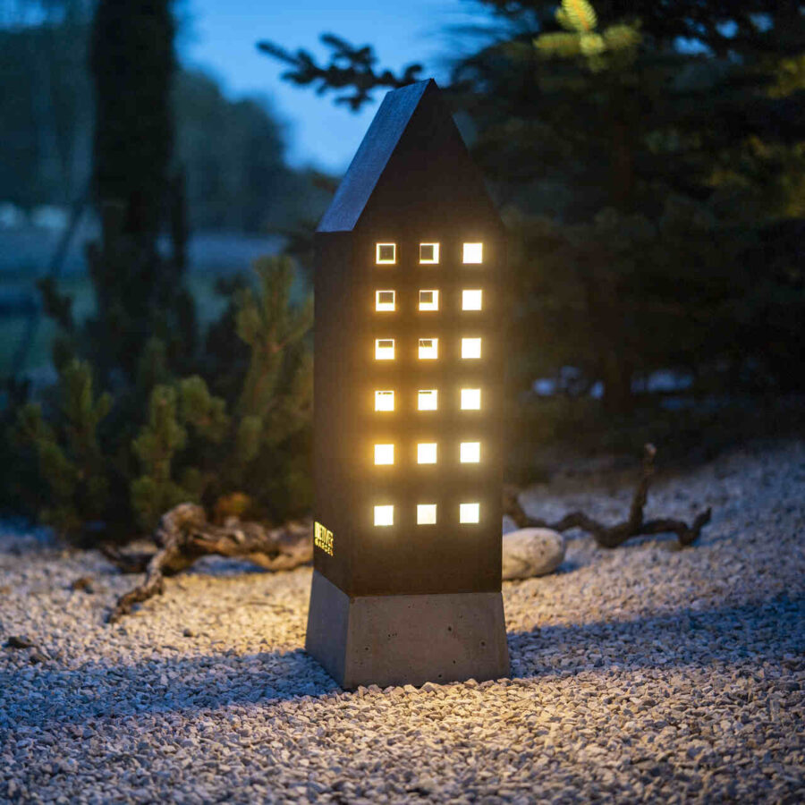 Lampion zewnętrzny mający formą kamienicy z wieloma kwadratowymi okienkami. Rozświetla wieczorem przestrzeń w ogrodzie.